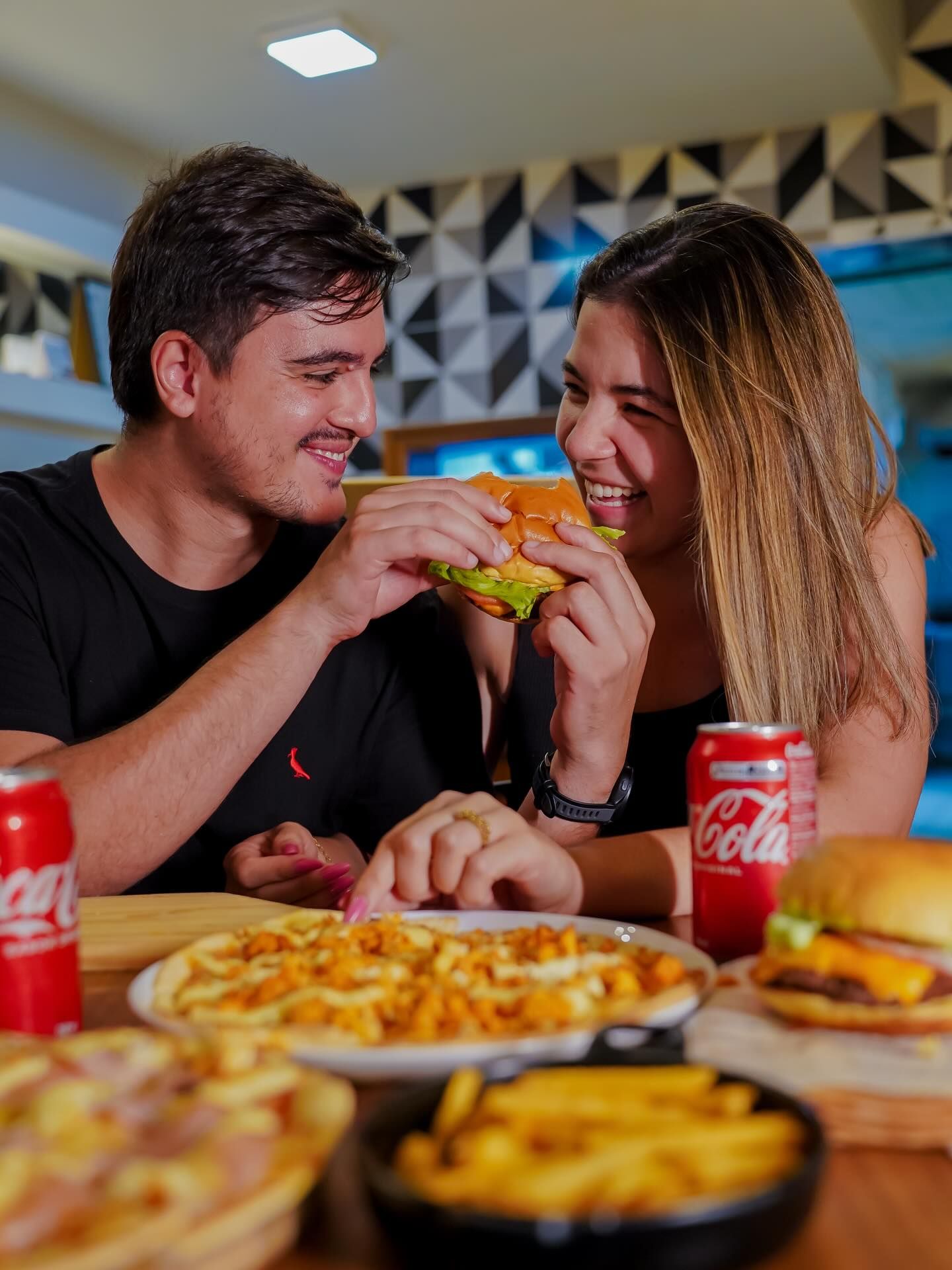 Mesa do salão da Co.Burg com a parede verde e o letreiro em neon