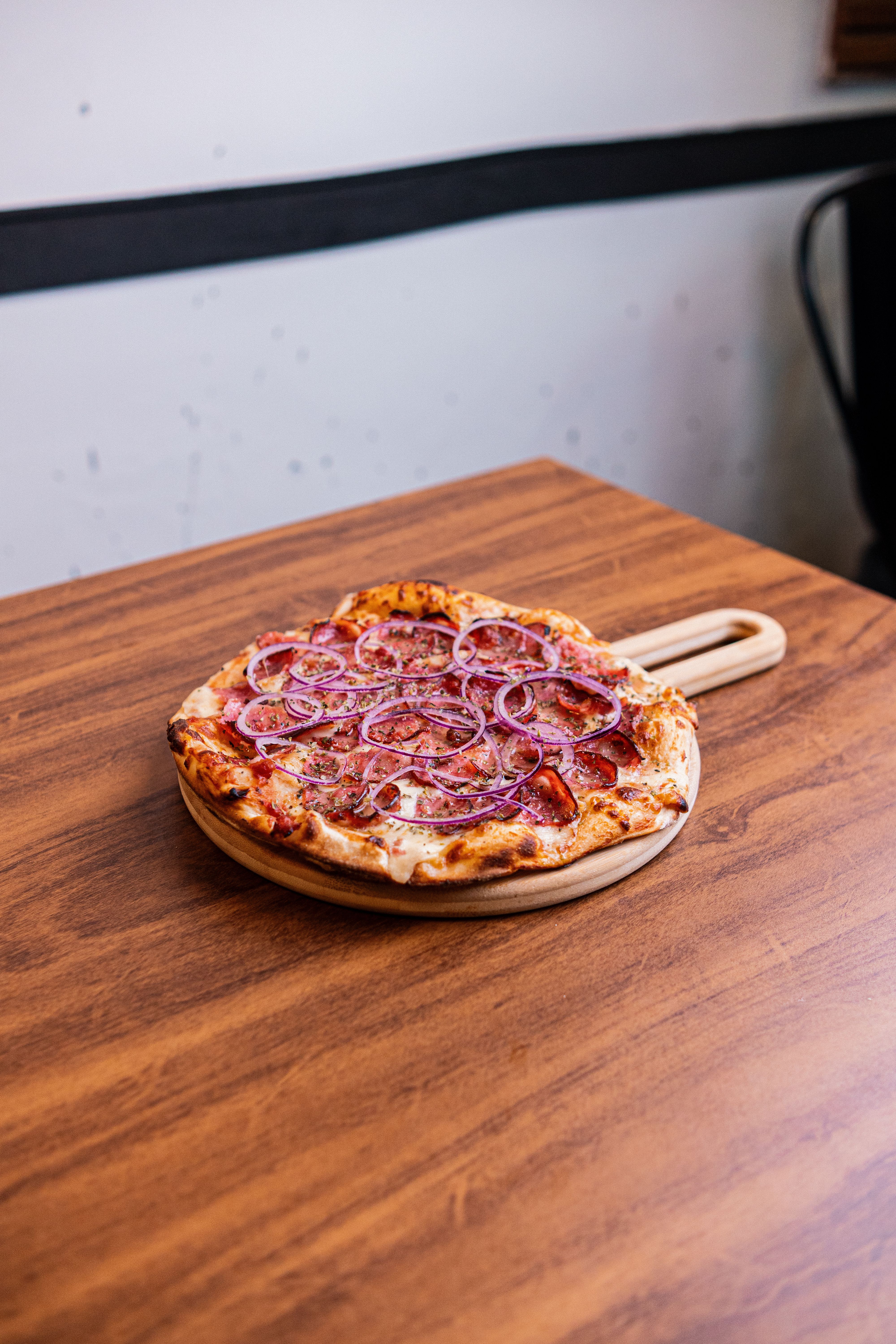 Pizza da Co.Burg com cebola roxa servida em tábua de madeira